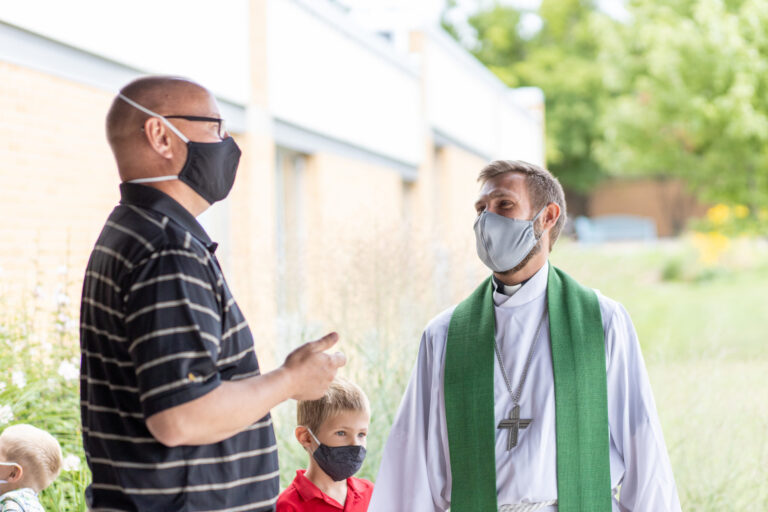 Masked pastor speaking with a masked church member