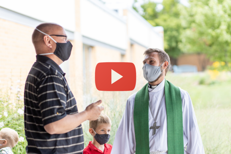 Masked pastor conversing with masked church member